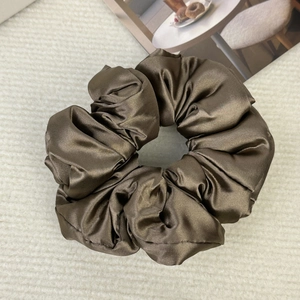 Detail of dark brown satin scrunchie with soft pleats on a textured background