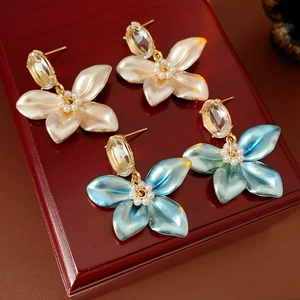 Detail of floral earrings with pearl petals and blue crystals on a wooden jewelry box