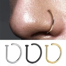 Macro detail of D-shaped stainless steel nose rings in silver, black and gold finish