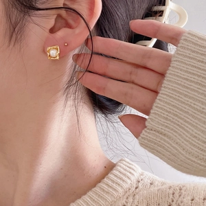 Close-up of elegant gold square frame pearl stud earrings worn by a model in warm light