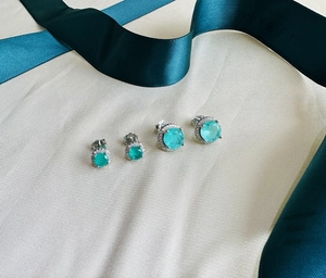 Macro detail of round halo earrings featuring emerald green stones on textured fabric