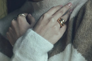 Close-up of a wide polished gold dome ring worn on finger with a cozy knit sweater background