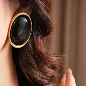 Retro oversized oval resin stud earrings in black and gold finish on female model