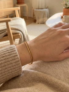 Detail view of a 18k gold double-layered flat snake chain and beaded bracelet on a wrist
