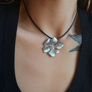 Detail of silver daisy flower pendant with zircon center on black leather cord