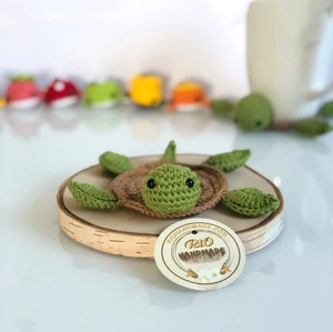 Close-up of handmade crochet turtle coaster with green head and brown shell on wood base