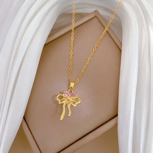 Detail of gold bow necklace with a pink heart gemstone on soft white silk fabric