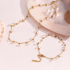 18K gold plated stainless steel necklace and bracelet set with white pearls on a pink surface