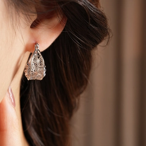 Detailed close-up of a hollow geometric cage earring in polished silver metal finish