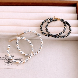 Detail of leather-wrapped hoop earrings in black and white with repeated NICE lettering