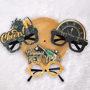 Three pairs of black and gold Happy New Year party glasses on a rustic wooden tray