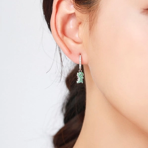 Detailed view of an S925 silver dinosaur earring with green zircons on a model's ear