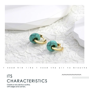 Close-up of golden hoop earrings with turquoise stones on a white textured backdrop