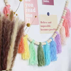 Bohemian garland featuring natural wood beads and colorful cotton tassels on a white wall