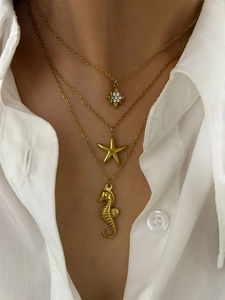 Détail de colliers superposés dorés avec pendentifs étoile de mer, hippocampe et étoile