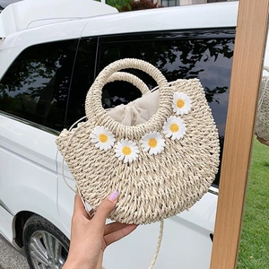 Detail der handgefertigten beigen Stroh-Eimertasche mit weißen floralen 3D-Gänseblümchen