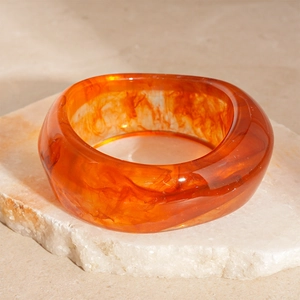 Detail of amber acrylic resin bangle with marble texture on a natural stone base