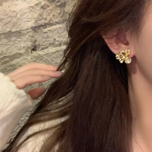 Close-up of golden flower stud earring with opal centerpiece worn by a model