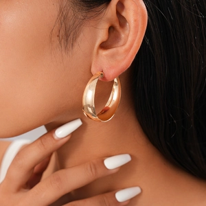 Close-up of a wide polished gold hoop earring worn by a model for a stylish look