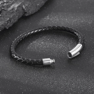 Detail of black woven leather bracelet with silver magnetic buckle on stone background
