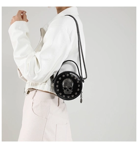 Close-up of black round leather crossbody bag with skull charm and metal chain strap