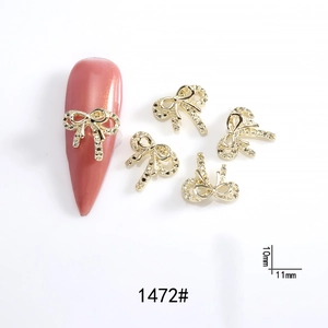 Detail of 11x10mm gold bow nail charms with rhinestones on pink almond fake nails