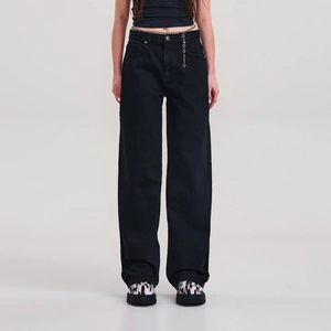 Détail du pantalon en denim noir à jambes larges avec une chaîne de taille en métal