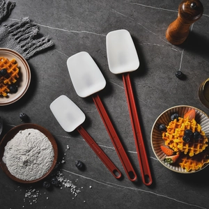 Three heat-resistant silicone spatulas with red handles on dark marble kitchen background
