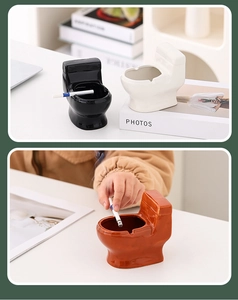 Ceramic toilet-shaped ashtrays in black white and orange colors on a modern desk