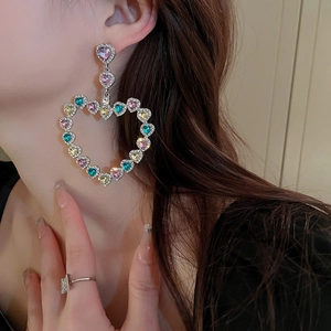 Détail de grandes boucles d'oreilles cœur ajourées avec cristaux colorés sur modèle