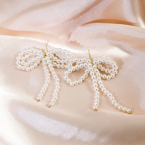 Detailed macro shot of long pearl bow earrings with tassels on champagne silk fabric