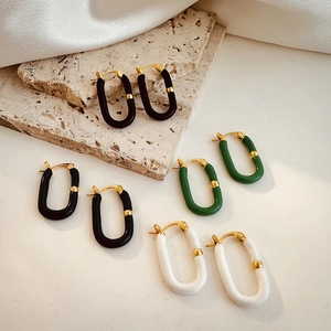 Detailed close-up of U-shaped gold earrings with black, green and white enamel finish