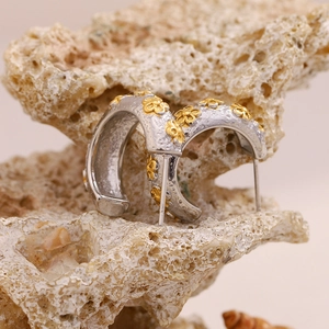 Detailed shot of two-tone C-shaped earrings with gold floral accents on textured rock