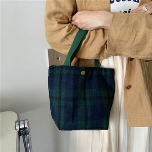 Detailed close-up of dark green plaid wool handbag with golden metal clasp and woven handle
