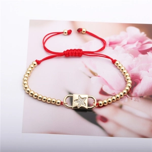 Makro-Detail von rotem Stoffarmband mit Goldperlen und Stern-Zirkonia-Anhänger auf Karte