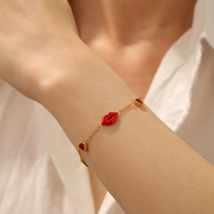 Detailed view of a gold chain bracelet with red enamel lips and heart zircon charms