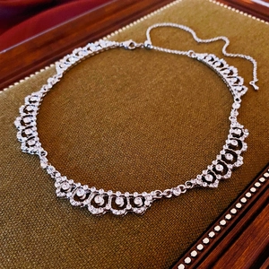 Macro detail of silver lace pattern necklace with crystals on green velvet display