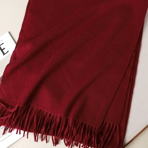 Detail shot of a soft wine red cashmere scarf with elegant fringe on a beige background