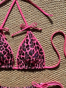 Close-up of pink leopard print bikini top with lace-up ties and bow detail on woven mat