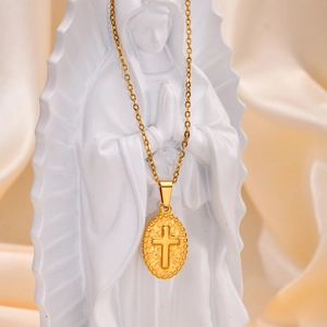 Detailed close-up of a golden oval cross pendant necklace displayed on a white statue