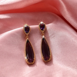 Close-up of vintage gold water drop earrings with purple zircon on pink satin background