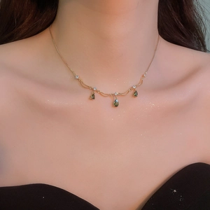 Dettaglio della collana placcata in oro con gemma a goccia verde sul collo della modella