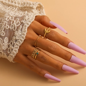 Detail of elegant gold-toned moon and crown ring set worn by a model on almond background