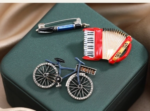 Detail of vintage bicycle, accordion and pen brooches with rhinestones on silk