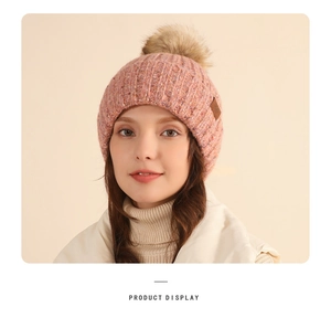 Detailed knit texture of pink and purple beanie with faux fur pom and leather tag