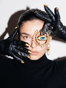 Detailed view of vintage gold evil eye brooch with crystals on black leather gloves