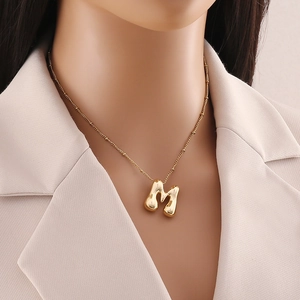 Dettaglio della collana con ciondolo a lettera M dorata su catena a sfere indossata da modella