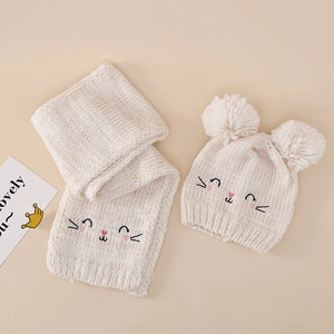 Close-up of baby knit hat and scarf set with cute cat embroidery and double faux fur pom-poms