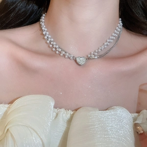 Close-up of double-layer pearl necklace with a shimmering heart pendant on a model