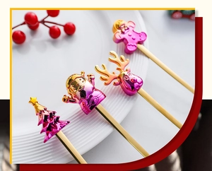 Detail view of 4 golden Christmas spoons with colorful festive toppers on a white ceramic plate